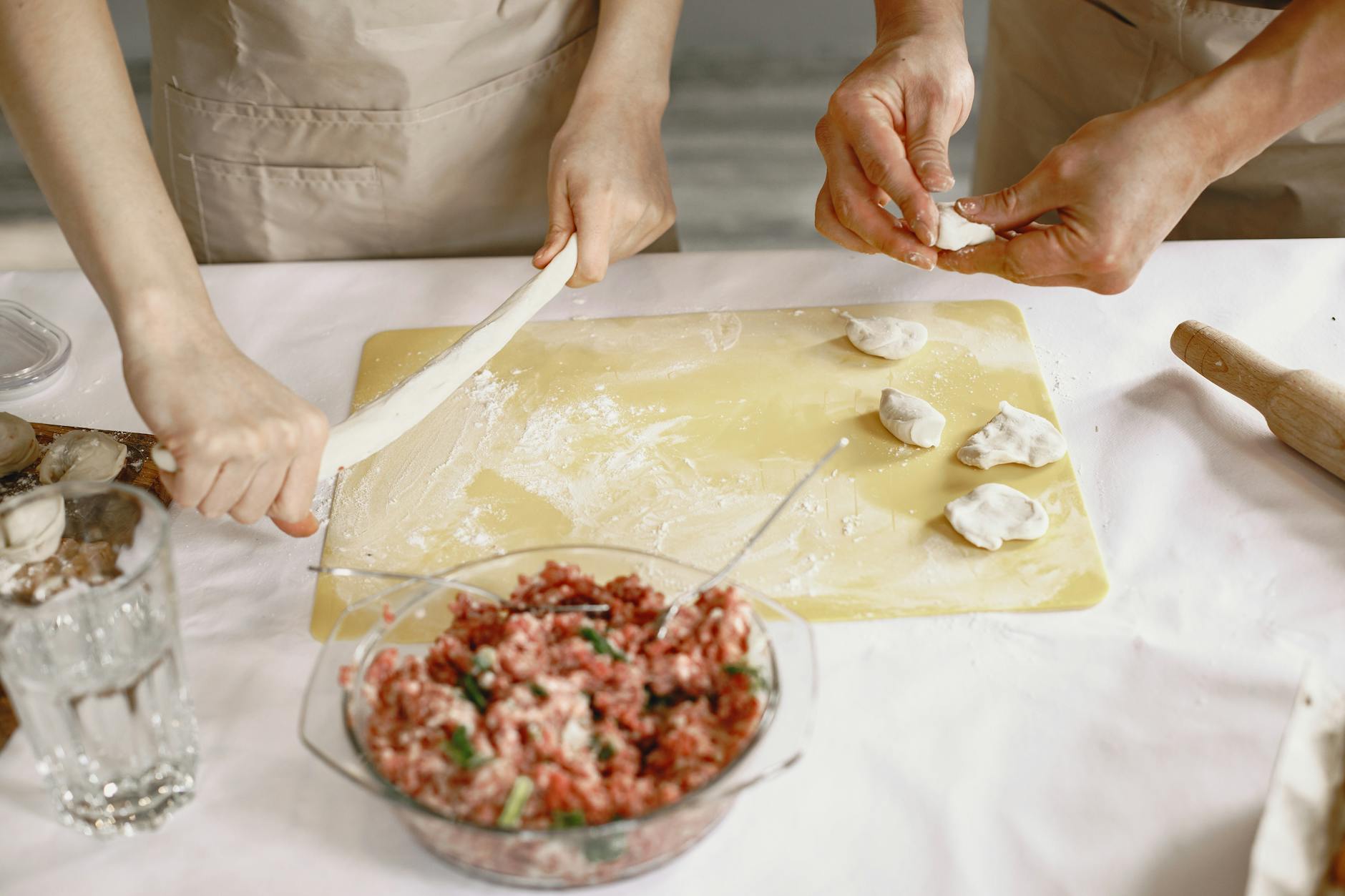 Dłonie lepią domowe pierogi z mięsnym farszem na kuchennym blacie