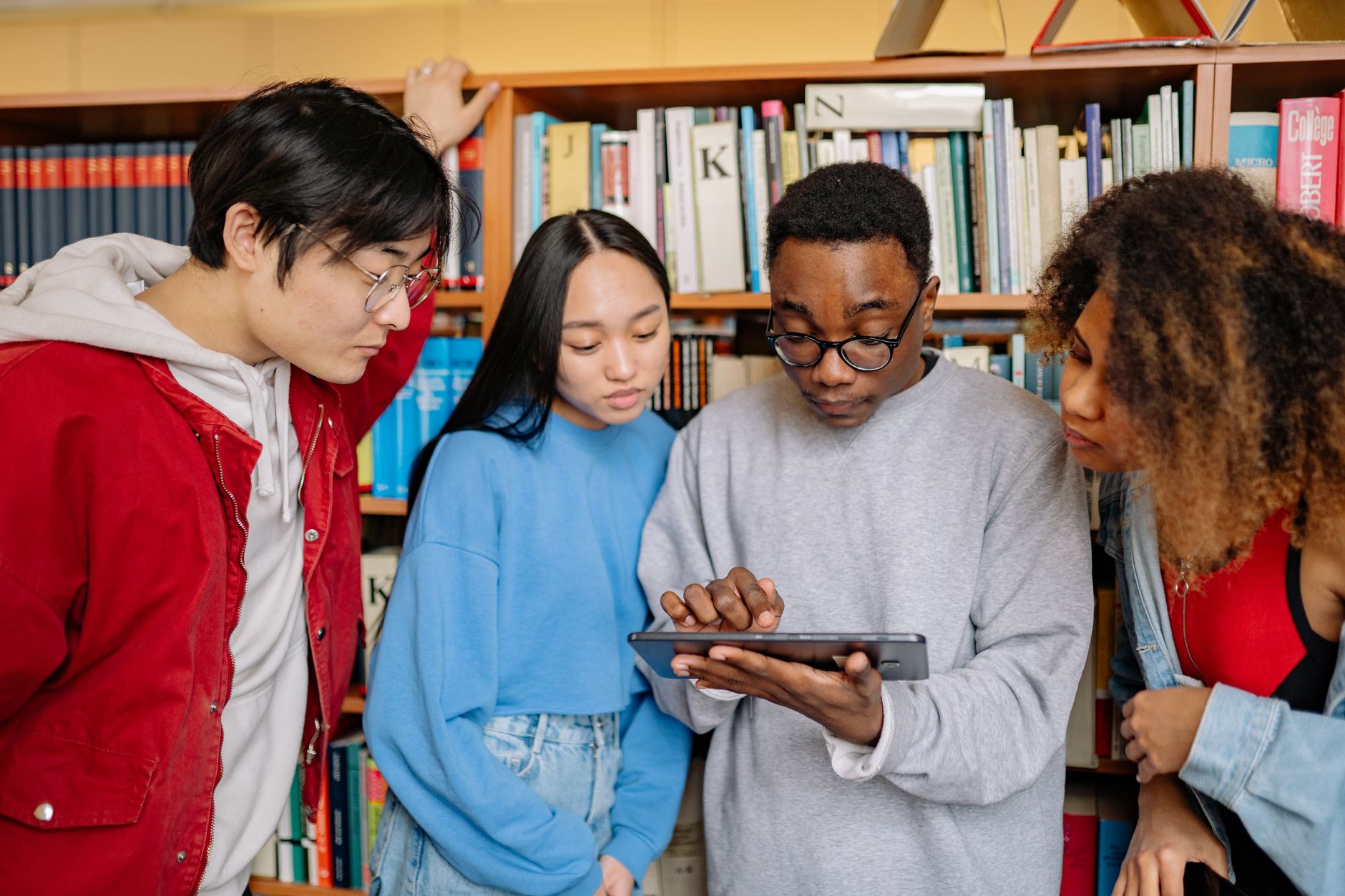 Studenci pracują wspólnie przy tablecie w bibliotece pełnej książek